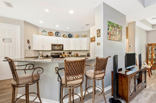 kitchen with kitchen peninsula, appliances with stainless steel finishes, light wood-type flooring, a breakfast bar, and white cabinetry