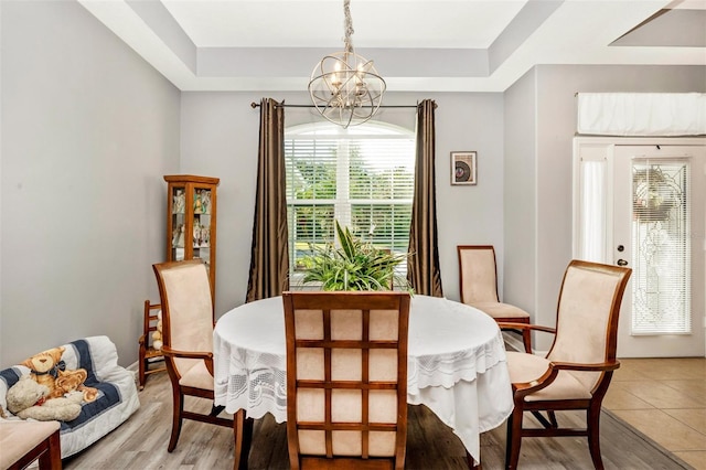 dining room featuring a tray ceiling, an inviting chandelier, and light wood-type flooring