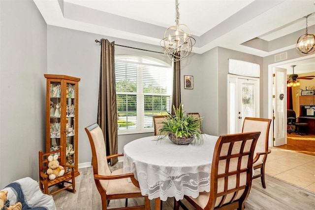 dining space featuring ceiling fan with notable chandelier, light hardwood / wood-style floors, and a raised ceiling