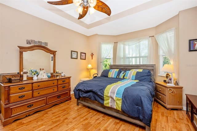 bedroom with a tray ceiling, multiple windows, ceiling fan, and light hardwood / wood-style floors