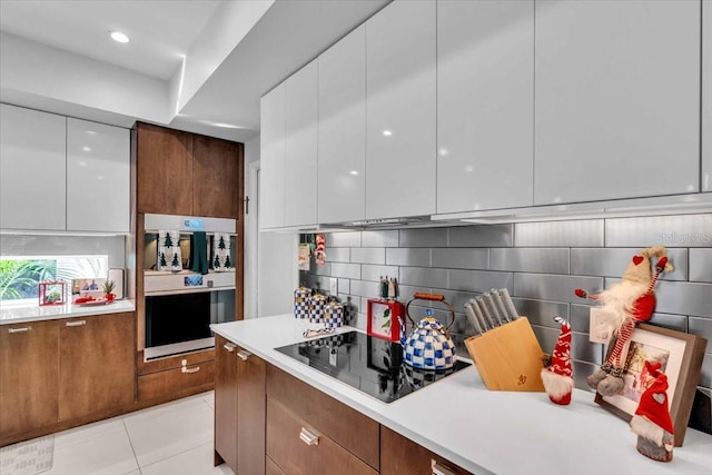 kitchen featuring white cabinets, black electric stovetop, decorative backsplash, and light tile patterned floors