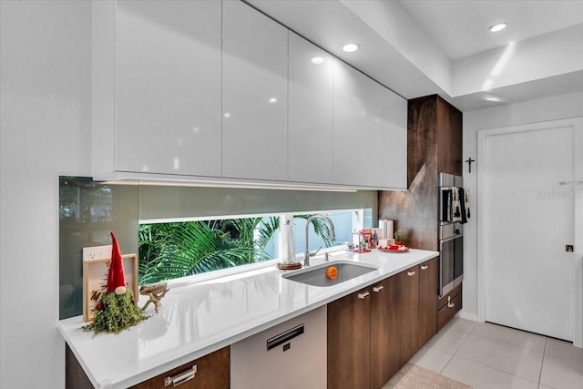 kitchen featuring dark brown cabinetry, sink, oven, and light tile patterned flooring