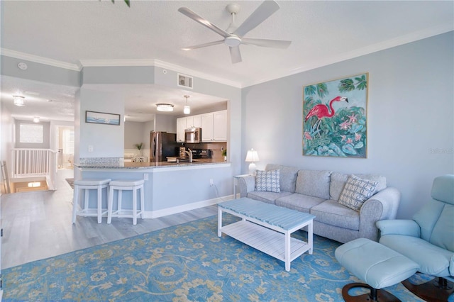 living room with light wood-type flooring, ornamental molding, a textured ceiling, ceiling fan, and sink