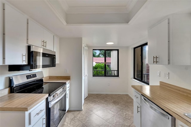 kitchen featuring white cabinets, ornamental molding, light tile patterned floors, a tray ceiling, and stainless steel appliances