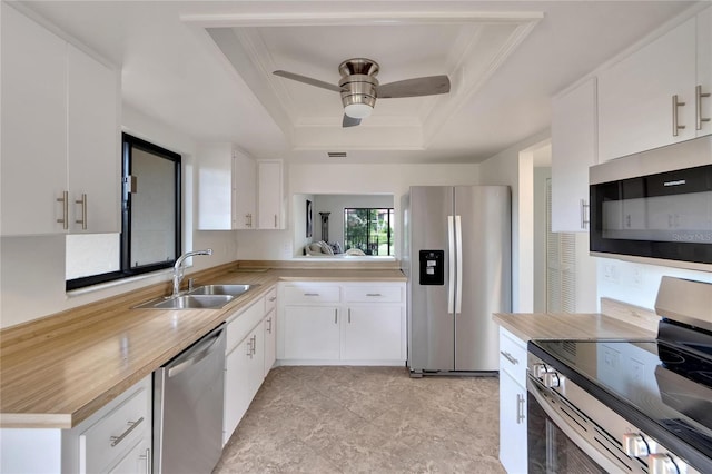 kitchen with appliances with stainless steel finishes, a tray ceiling, ceiling fan, sink, and white cabinetry