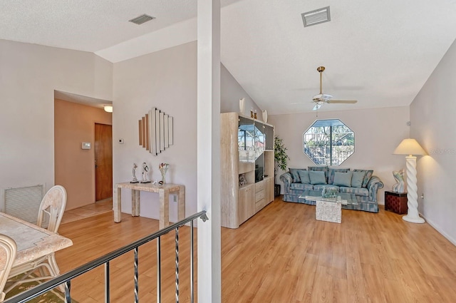 living room with lofted ceiling, ceiling fan, light wood-type flooring, and a textured ceiling