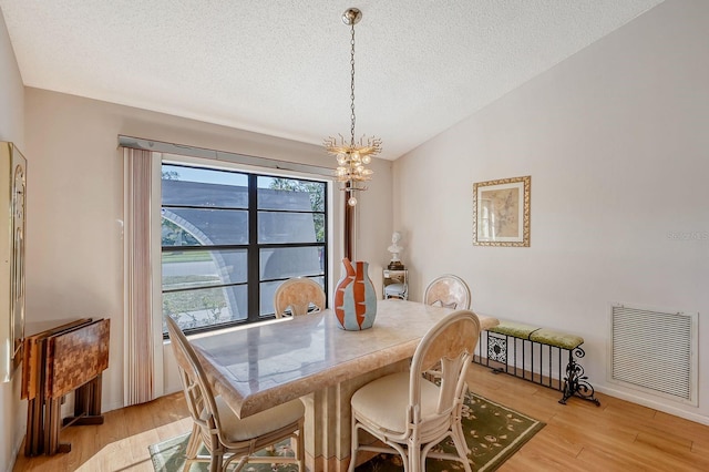 dining room featuring a textured ceiling, light hardwood / wood-style flooring, a chandelier, and vaulted ceiling