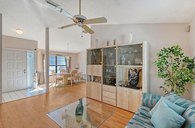 living room with hardwood / wood-style flooring, ceiling fan, a textured ceiling, and vaulted ceiling