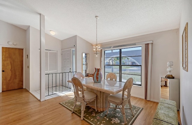 dining room with high vaulted ceiling, light hardwood / wood-style floors, a textured ceiling, and a notable chandelier