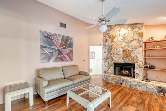 living room featuring ceiling fan, a stone fireplace, wood-type flooring, and vaulted ceiling