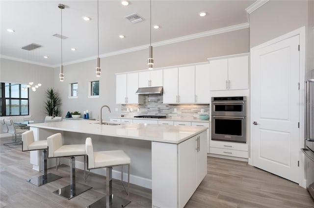 kitchen featuring a kitchen island with sink, sink, stainless steel appliances, and decorative light fixtures