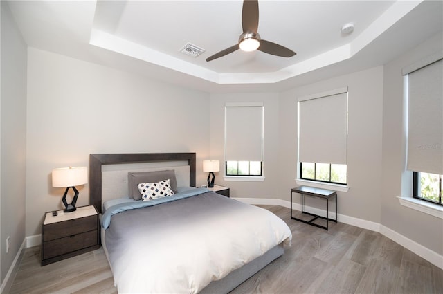 bedroom with a tray ceiling, multiple windows, light hardwood / wood-style floors, and ceiling fan