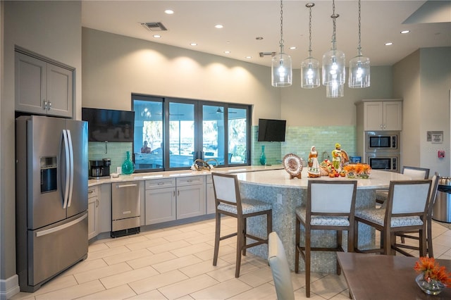 kitchen with appliances with stainless steel finishes, a kitchen breakfast bar, a center island, gray cabinets, and hanging light fixtures