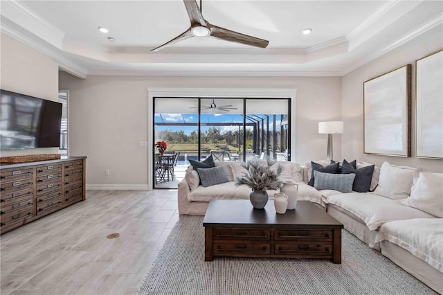 living room featuring ceiling fan, a raised ceiling, ornamental molding, and light wood-type flooring