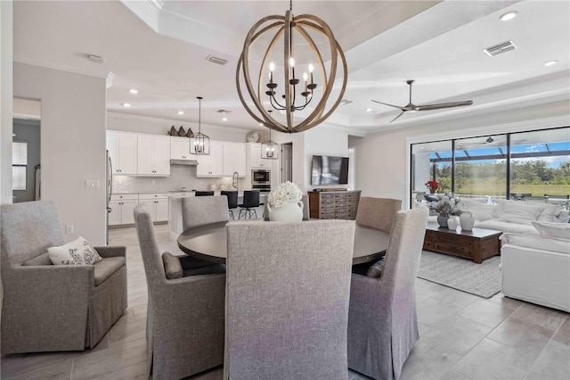 tiled dining area featuring ceiling fan with notable chandelier, ornamental molding, sink, and a tray ceiling