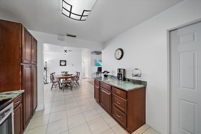 kitchen with light tile patterned floors, stone countertops, and stainless steel range oven