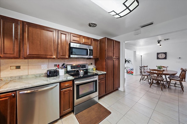 kitchen with tasteful backsplash, light stone counters, light tile patterned floors, and stainless steel appliances