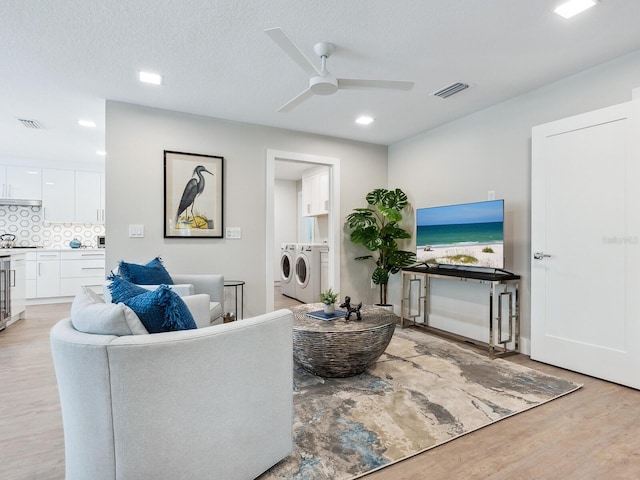 living room with a textured ceiling, ceiling fan, beverage cooler, light hardwood / wood-style flooring, and independent washer and dryer