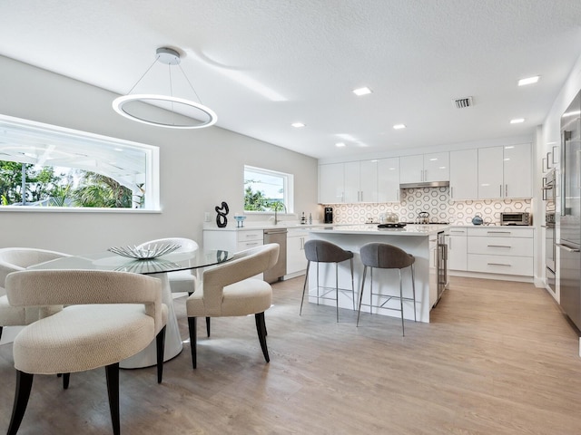 kitchen featuring pendant lighting, backsplash, white cabinets, stainless steel dishwasher, and light wood-type flooring