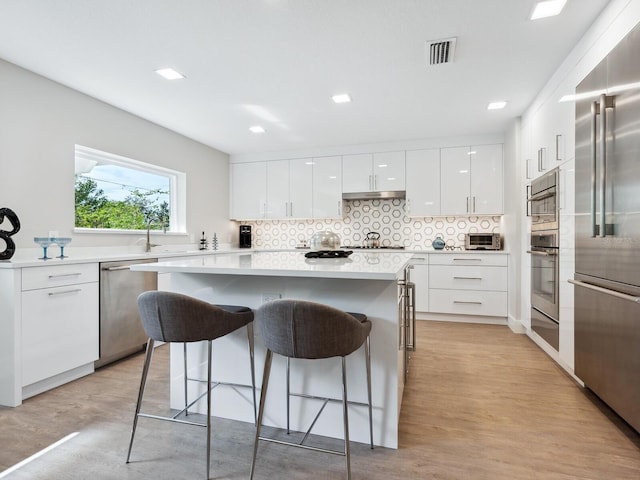 kitchen with decorative backsplash, appliances with stainless steel finishes, light wood-type flooring, a kitchen bar, and white cabinets