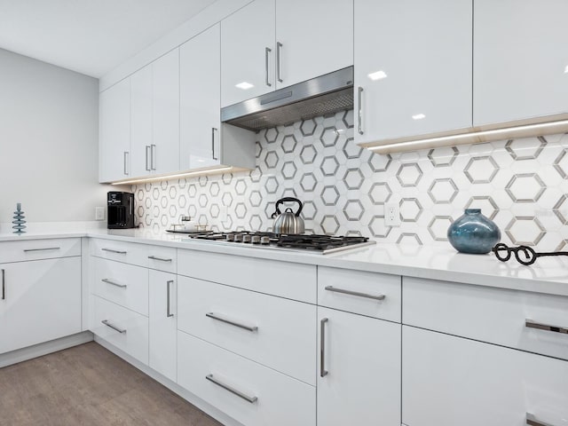 kitchen with stainless steel gas stovetop, white cabinets, light wood-type flooring, tasteful backsplash, and light stone counters