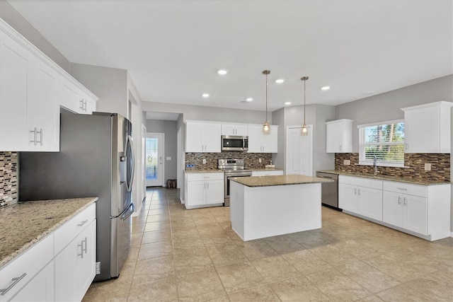 kitchen with pendant lighting, a center island, light stone countertops, white cabinetry, and stainless steel appliances