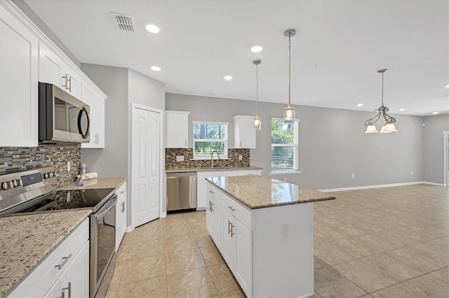 kitchen with a center island, light stone counters, decorative light fixtures, white cabinets, and appliances with stainless steel finishes