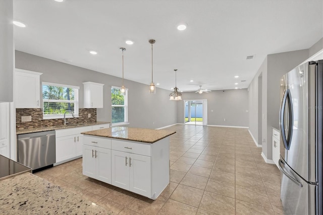 kitchen with white cabinetry, ceiling fan, a center island, light stone countertops, and appliances with stainless steel finishes