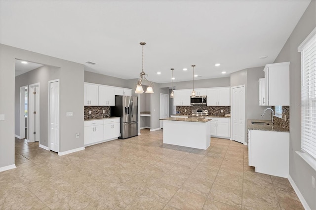 kitchen with white cabinetry, stainless steel appliances, dark stone counters, decorative light fixtures, and a kitchen island