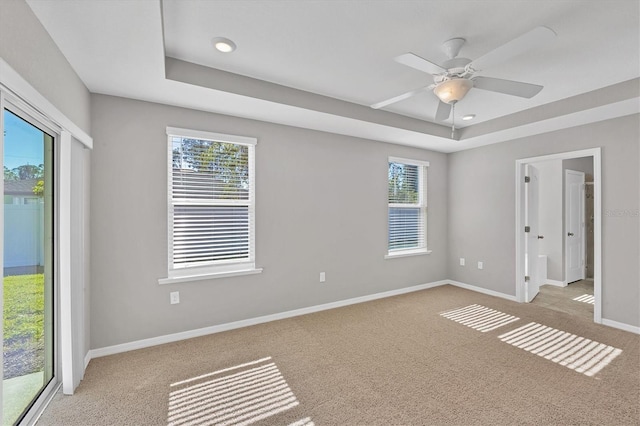 empty room featuring a raised ceiling, light carpet, plenty of natural light, and ceiling fan