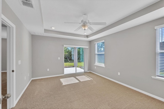 empty room with carpet flooring, a raised ceiling, and ceiling fan