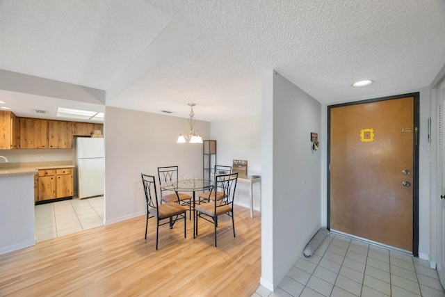 dining space with light hardwood / wood-style floors, a textured ceiling, and a notable chandelier