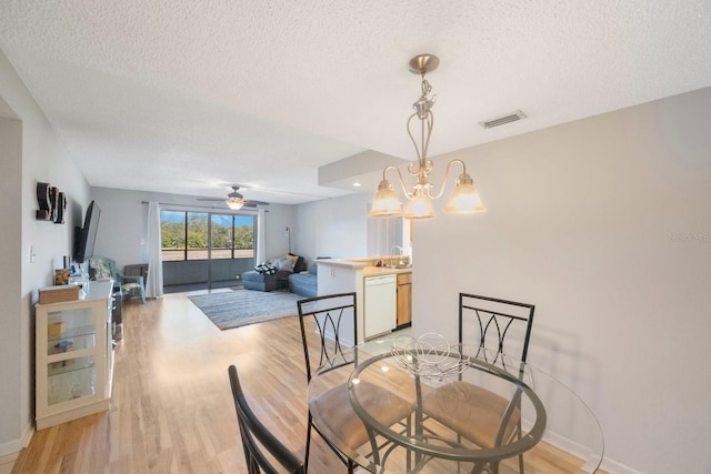 dining room with a textured ceiling, ceiling fan with notable chandelier, light hardwood / wood-style flooring, and sink