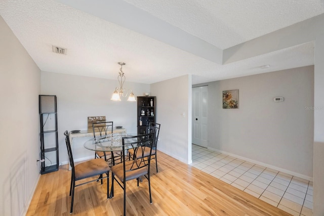 dining space with a notable chandelier, light hardwood / wood-style floors, and a textured ceiling