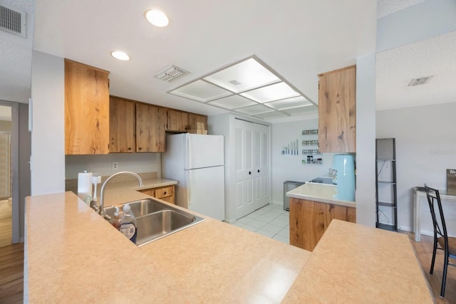 kitchen featuring kitchen peninsula, white fridge, light hardwood / wood-style floors, and sink