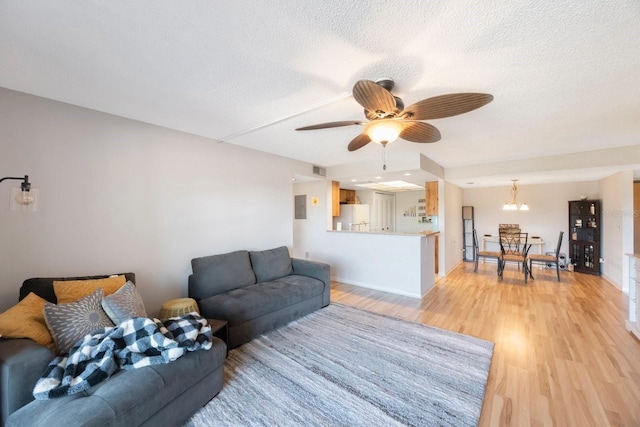 living room featuring ceiling fan with notable chandelier, a textured ceiling, and light hardwood / wood-style flooring