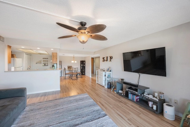 living room with a textured ceiling, light wood-type flooring, and ceiling fan