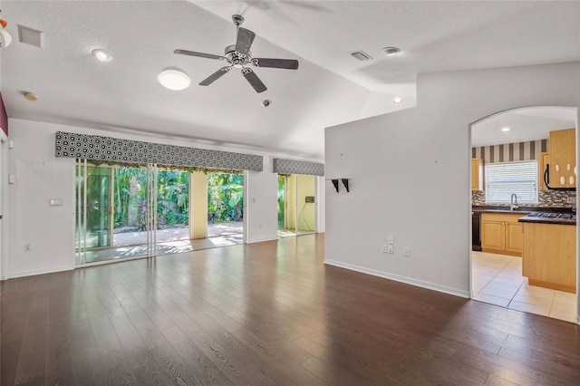 unfurnished living room with a textured ceiling, ceiling fan, vaulted ceiling, and light wood-type flooring