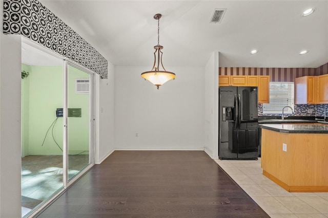 kitchen with light brown cabinetry, light wood-type flooring, tasteful backsplash, black refrigerator with ice dispenser, and decorative light fixtures