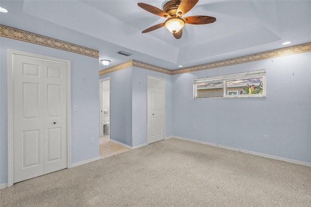 unfurnished bedroom featuring a tray ceiling, ceiling fan, and light carpet