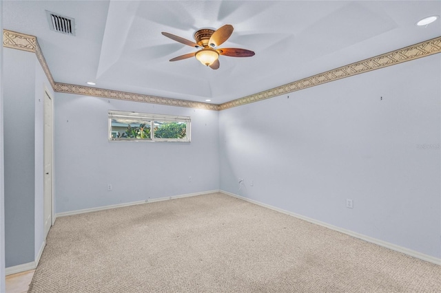 spare room with a raised ceiling, ceiling fan, and light colored carpet