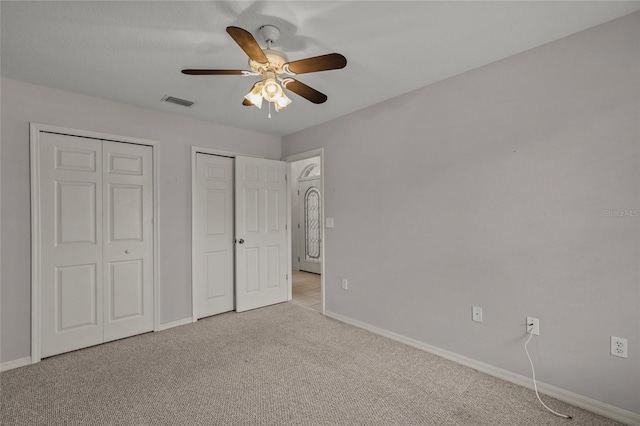 unfurnished bedroom featuring light colored carpet, ceiling fan, and multiple closets