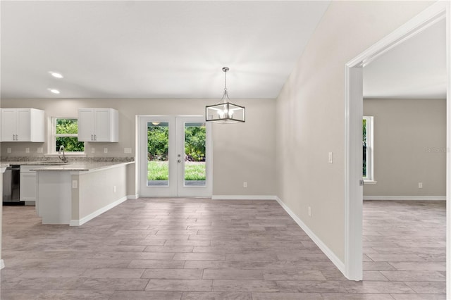 kitchen with light wood-type flooring, stainless steel dishwasher, light stone counters, white cabinetry, and hanging light fixtures