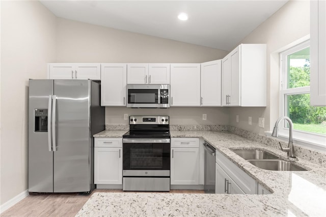 kitchen with sink, vaulted ceiling, light stone countertops, appliances with stainless steel finishes, and white cabinetry