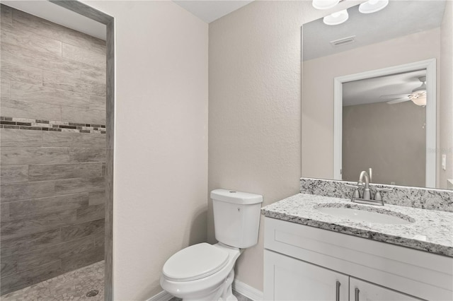 bathroom with a tile shower, ceiling fan, vanity, and toilet