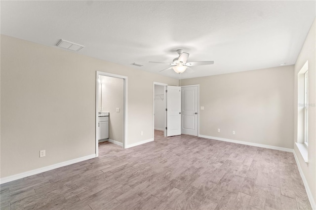 unfurnished bedroom with a walk in closet, ceiling fan, light wood-type flooring, connected bathroom, and a closet