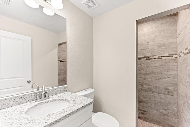 bathroom featuring a tile shower, vanity, and toilet