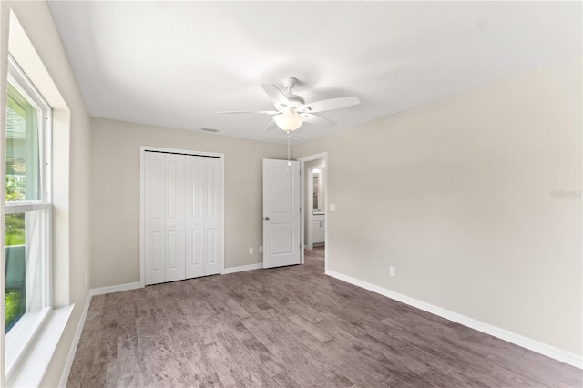 unfurnished bedroom featuring a closet, multiple windows, ceiling fan, and hardwood / wood-style floors