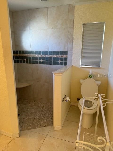 bathroom featuring tile patterned floors, toilet, and a tile shower