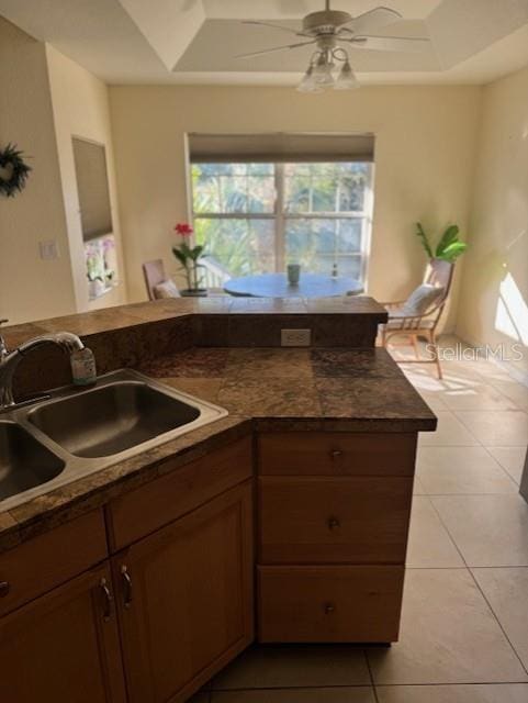 kitchen with light tile patterned floors, a raised ceiling, ceiling fan, and sink